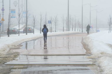 Minsk, Beyaz Rusya - 13 Mart 2018: siluetleri ile su birikintileri, ıslak bir kaldırımda çekip iki kişinin arkasından görüntüleyin. Erken baharda kötü hava koşulları. Güçlü sis
