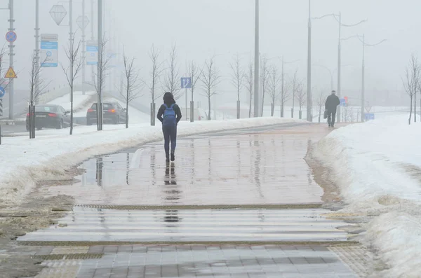 Minsk, Beyaz Rusya - 13 Mart 2018: siluetleri ile su birikintileri, ıslak bir kaldırımda çekip iki kişinin arkasından görüntüleyin. Erken baharda kötü hava koşulları. Güçlü sis
