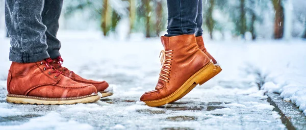Πόδια ζευγαριού σε ένα χιονισμένο πεζοδρόμιο με καφέ μπότες Royalty Free Φωτογραφίες Αρχείου