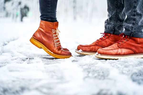 Pieds d'un couple sur un trottoir enneigé en bottes brunes Images De Stock Libres De Droits