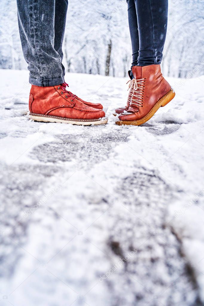 Feet of a couple on a snowy sidewalk in brown boots