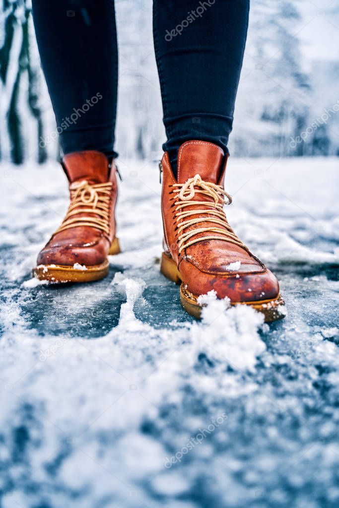 Feet of a woman on a snowy sidewalk in brown boots