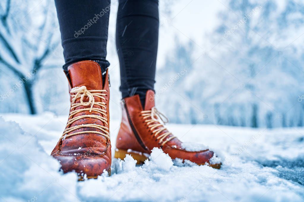 Feet of a woman on a snowy sidewalk in brown boots