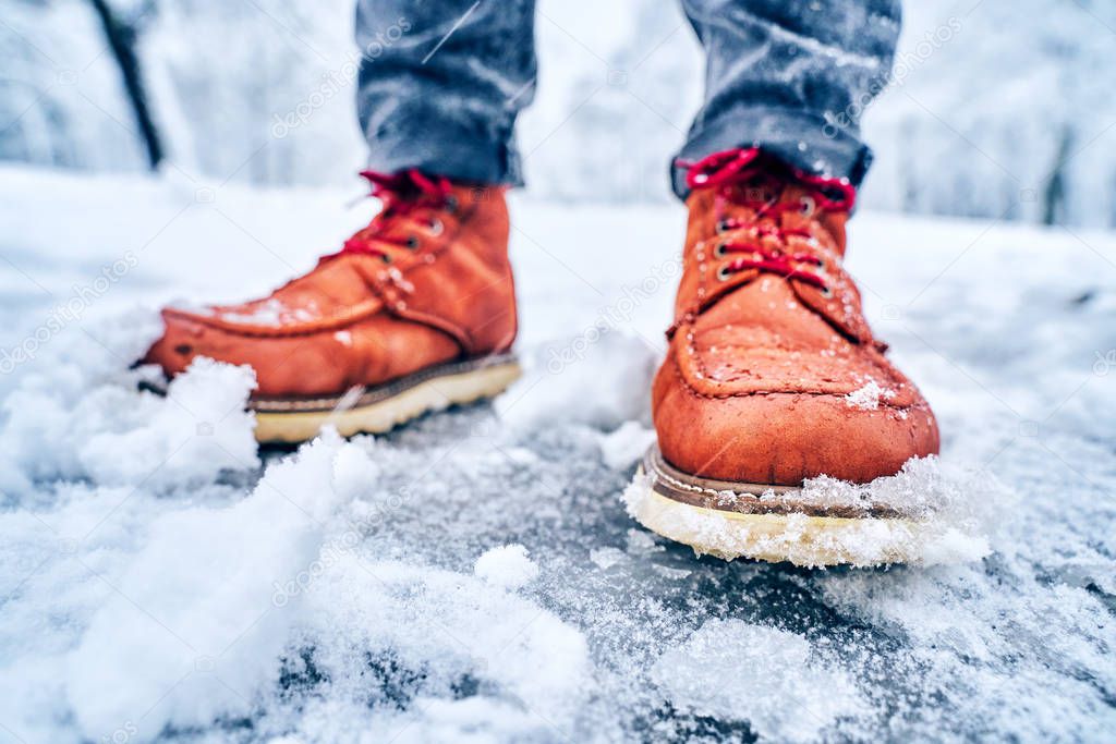 Feet of a man on a snowy sidewalk in brown boots