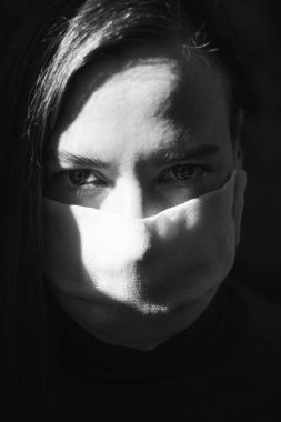 Gazlı bez maskeli bir kadının gözleri kameraya yakından bakıyor. Kendi sağlığınızı viral enfeksiyondan korumak için. Coronavirus konsepti. Kontrast aydınlatma arkaplanı.