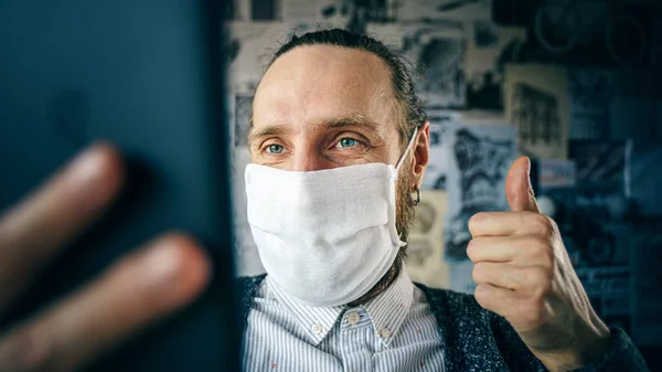 Portrait of a bearded man in a gauze mask, who talking remotely using tablet via video conference. Preventive protection of your own health from viral infection. Remote communication during an epidemic concept. Thumb up
