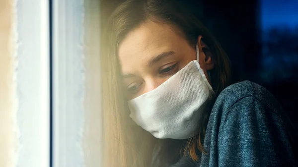 A woman in a gauze mask looks through the window. Anti-virus home isolation concept. Protect your health during the epidemic.