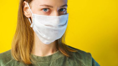 Sarı arka planda gazlı bez maskeli bir kadının portresi kameraya bakıyor. Kendi sağlığınızı viral enfeksiyondan korumak için. Coronavirus konsepti.