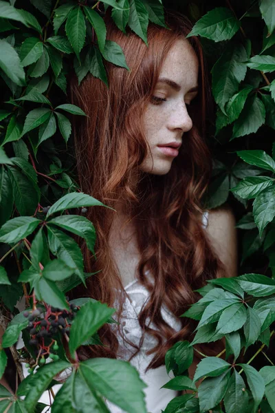 Mooi meisje met rode haren in groene bladeren — Stockfoto
