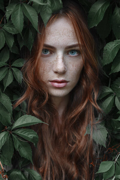 Красивая девушка с рыжими волосами в зеленых листьях
