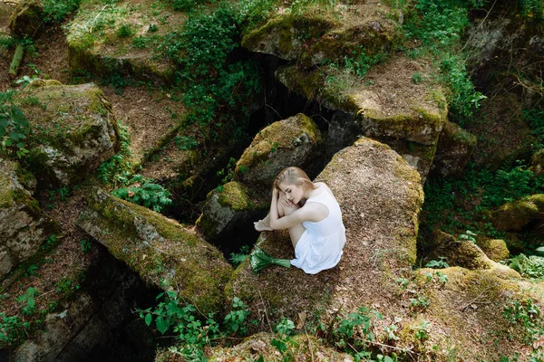 Девушка в белом платье на больших скалах с лилиями — стоковое фото