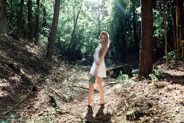 Mädchen mit einem Blumenstrauß und einem weißen Kleid in einem sonnigen Wald — Stockfoto