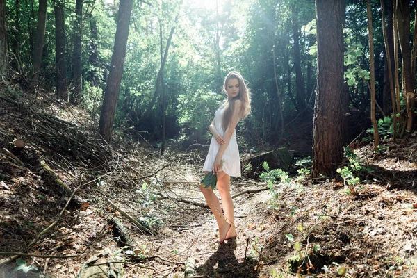 Menina com um buquê de flores e um vestido branco em uma floresta ensolarada — Fotografia de Stock