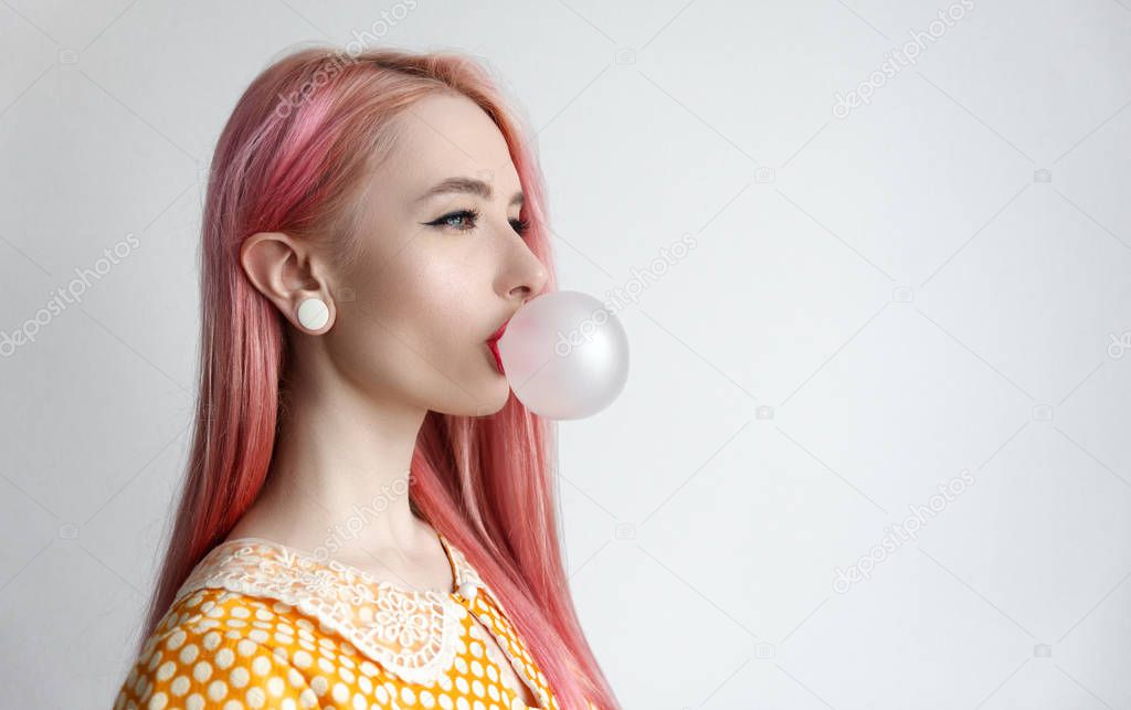 The girl with the pink hair is blowing bubble gum