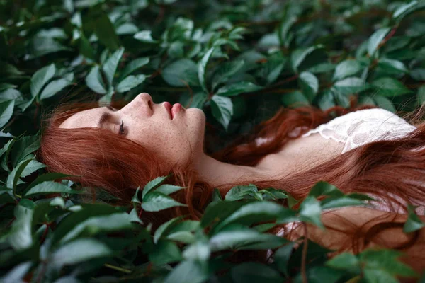 Девушка с рыжими волосами лежит среди зеленых листьев — стоковое фото