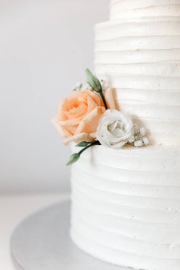 Çiçek ve yapraklarla süslenmiş beyaz kremalı düğün pastası.
