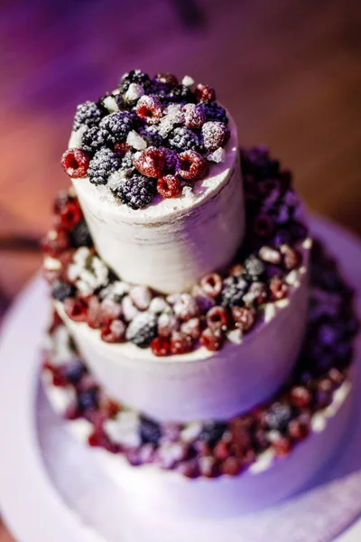 Purple wedding three-tier cake decorated with raspberries and berries closeup