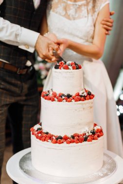 Böğürtlenlerle süslenmiş düğün pastası bıçakla kesilmiş damat takım elbiseli ve gelin.