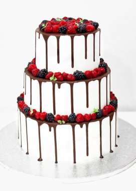 Beyaz arkaplanda beyaz krema ve taze dutlarla süslenmiş düğün pastası.