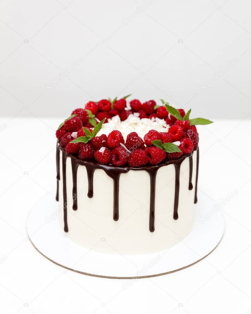 Beautiful cake decorated with melting chocolate and fresh raspberries on a white background