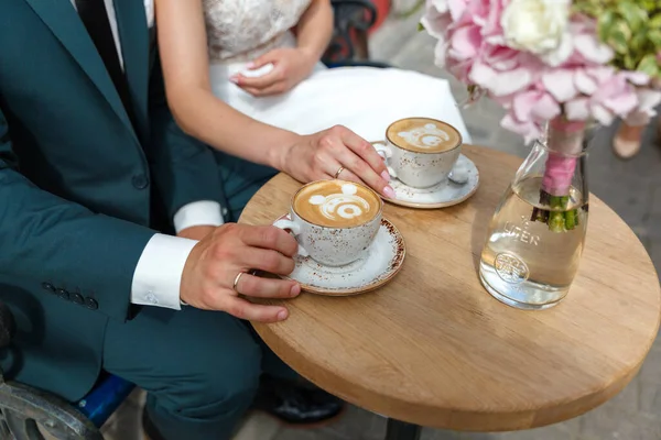 Couple in wedding dresses at a table in a cafe with coffee mugs, closeup no face