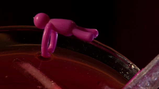 Copo de cocktail decorado com pequena boneca de plástico, fundo preto — Vídeo de Stock