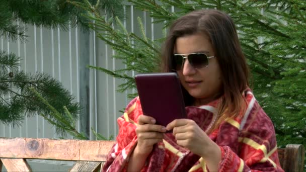 Дівчина в сонцезахисних окулярах і теплий плоский читати електронну книгу і пити чай, а потім встати — стокове відео