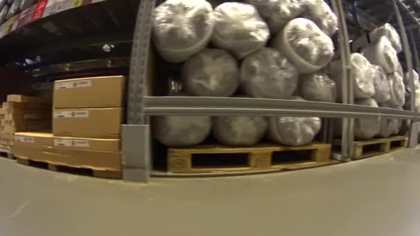 Meubelen winkel klant gaan met zijn aankoop tussen planken met kartonnen dozen en verpakte matrassen, onderste weergave — Stockvideo