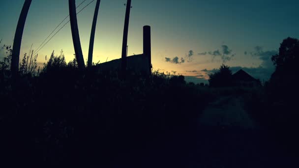 Silueta de postes de teléfono y hierba alta en el camino a la granja abandonada, tiro al atardecer de verano — Vídeo de stock