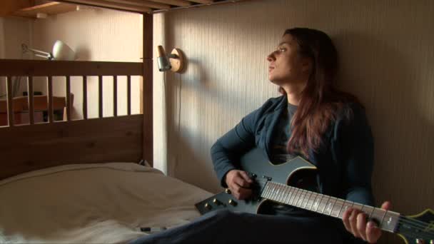 Девушка играет на гитаре дома на двухъярусной кровати — стоковое видео