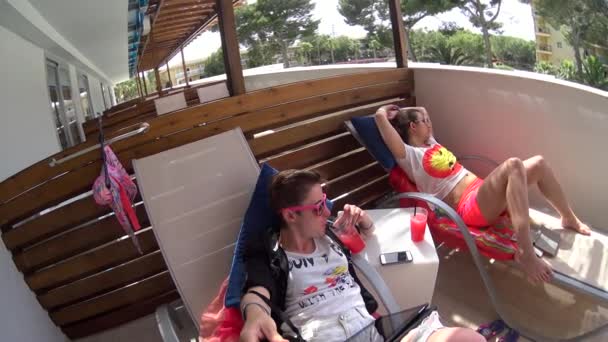 Zwei lesbische Mädchen mit Sonnenbrille liegen auf Liegestühlen auf der Balkonterrasse des Hotels, junge Frau schläft nach dem Schwimmen auf der Liege mit roten Cocktails — Stockvideo