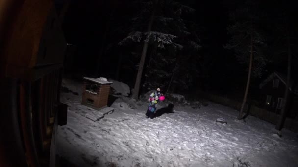 Девочка ночью делает снежного ангела во дворе — стоковое видео