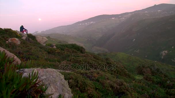Fille boire une bouteille assis sur un rocher de montagne, regarder lune du soir 