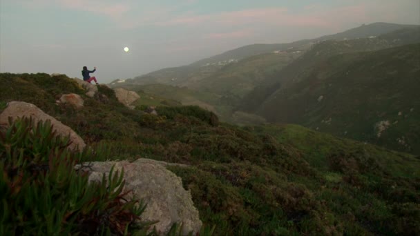 Chica tomando fotos en el teléfono celular, sentado en la roca de la montaña — Vídeo de stock