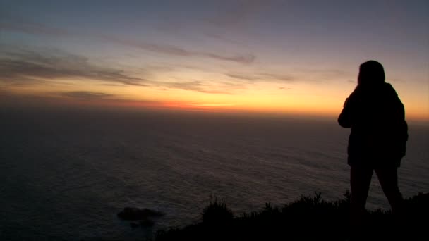 Meisje silhouet staand op berg top rotsmassief, kijken naar de zonsondergang over de Oceaan — Stockvideo