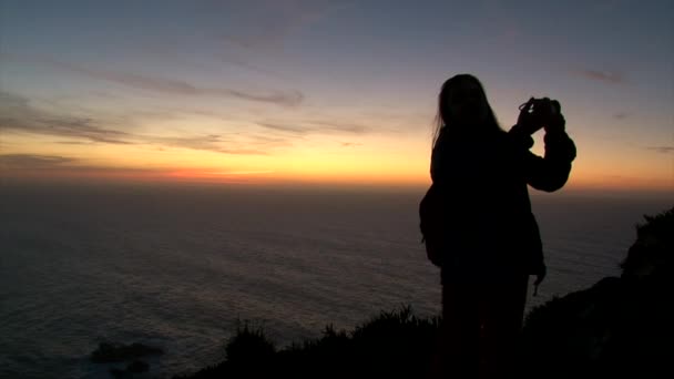 Silhouette de fille prenant selfie sur téléphone portable debout sur la falaise rocheuse océan — Video
