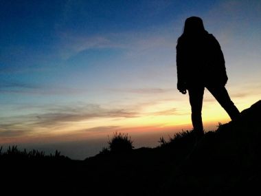 Dağ tepe cliff üzerinde duran, deniz suyu üzerinde gündoğumu izlerken kız siluet