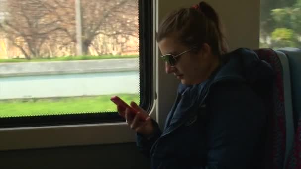 Hermosa chica en gafas de sol con teléfono inteligente sentado en el tren o autobús — Vídeos de Stock