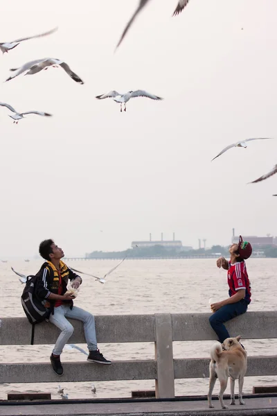 Dva mladí muži krmení ptáků ve vzduchu na Bang Pu přímořské. — Stock fotografie