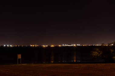 Küçük bir gece şehrinin ışıkları uzakta parlıyor. Parlak fenerleri olan bir şehrin gece manzarası.