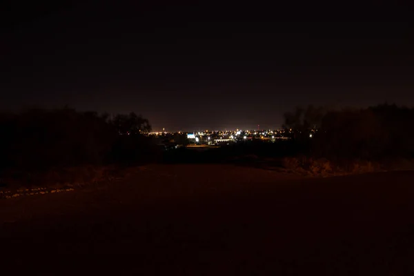 Küçük bir gece şehrinin ışıkları uzakta parlıyor. Parlak fenerleri olan bir şehrin gece manzarası.