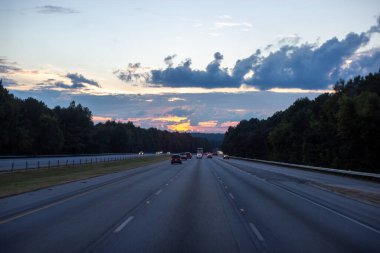 Gün batımında asfalt bir otoyolda arabalar gider. Bir yaz akşamında güzel bir yol.