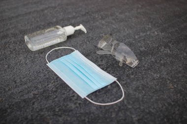 Coronavirus (covid-19) önleme ekipmanı. Tıbbi malzemeler. Gri asfaltta vücut sağlığı. Gri arka planda maske, dezenfektan ve gözlük