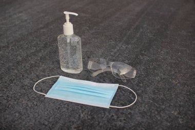 Coronavirus (covid-19) önleme ekipmanı. Tıbbi malzemeler. Gri asfaltta vücut sağlığı. Gri arka planda maske, dezenfektan ve gözlük