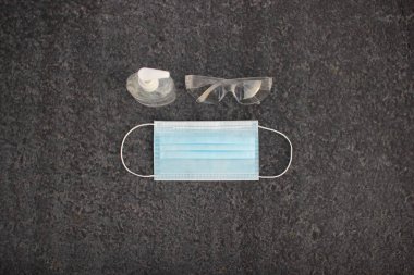 Coronavirus (covid-19) önleme ekipmanı. Tıbbi malzemeler. Gri asfaltta vücut sağlığı. Gri arka planda maske, dezenfektan ve gözlük
