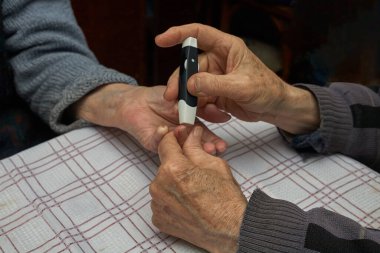 Evde kan örnekleri var. Yaşlı bir adam yaşlı bir kadına şırıngayla iğne batırır. Kan testi şeker için hızlı bir yöntem. Yatay çerçeve.