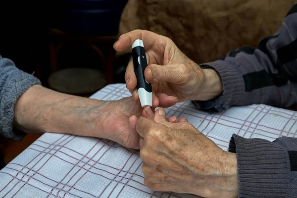 Evde şeker analizi çiti var. Yaşlı bir adam yaşlı bir kadına şırıngayla iğne batırır. Yatay çerçeve.