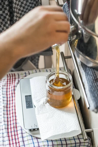 Beekeeper filling up the fresh golden new honey into glass jars on a scale scales — Stock Photo, Image