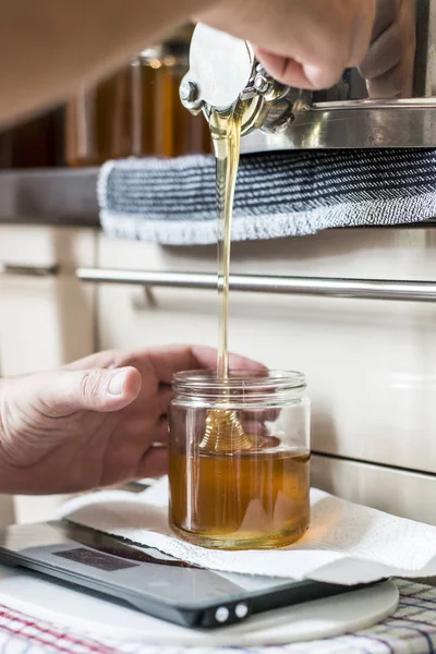 Beekeeper filling up the fresh golden new honey into glass jars on a scale scales — Stock Photo, Image
