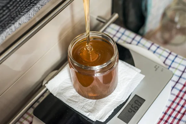 Apicultor enchendo o novo mel dourado fresco em frascos de vidro em uma balança — Fotografia de Stock